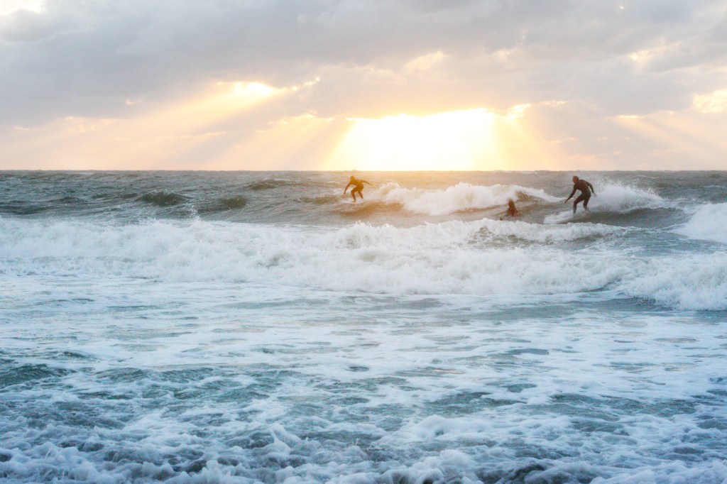 Surfers catch waves in rough surf with a dynamic sunset in the background at Sand Key, Florida.
