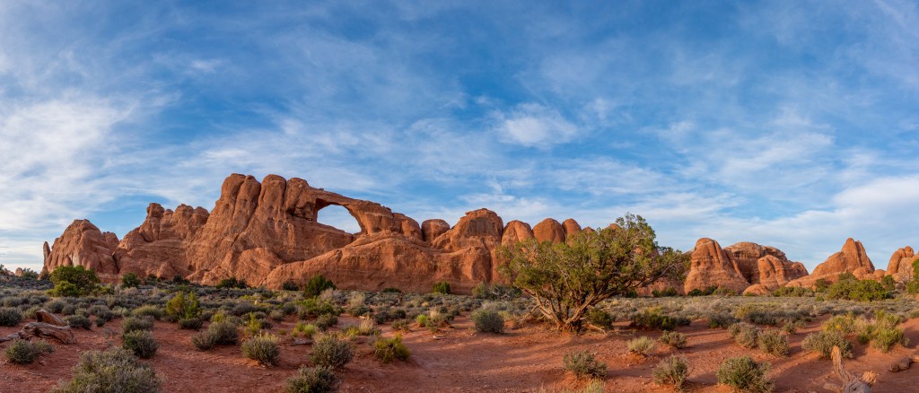 Spectacular red rocks point upwards in rounded pinnacles surrounding a large window (hole in the rock) in a desert setting with blue sky and wispy clounds. Skyline arch, Arches National Park.