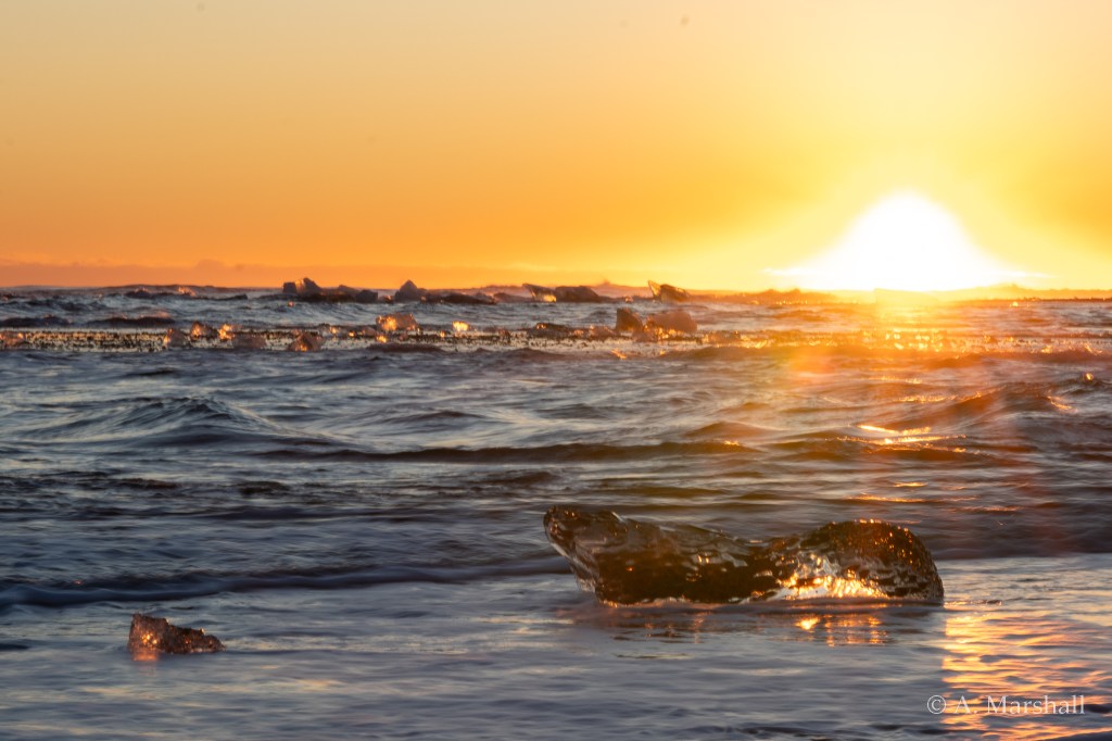 crystal clear pieces of ice drift along the waves in the sunset at Diamond beach, Iceland